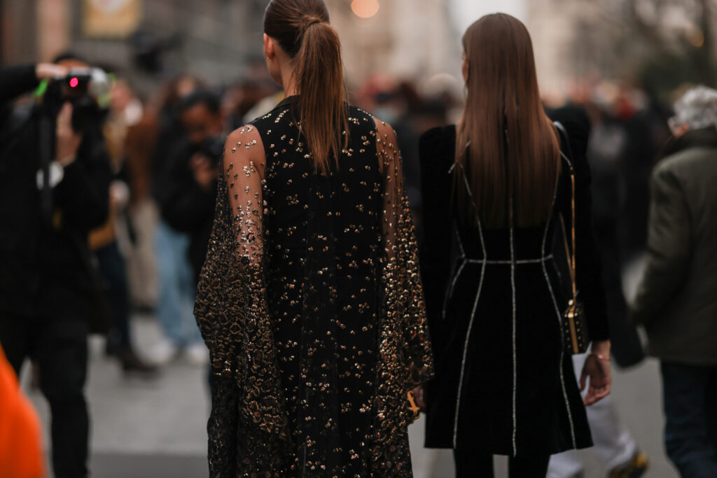 Снимката представя две жени в гръб облечени с официални черни кадифени рокли с лъщящи орнаменти