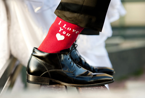 На снимката се виждат крака на мъж обут с червени чорапи с надпис i love you и черни лачени официални обувки