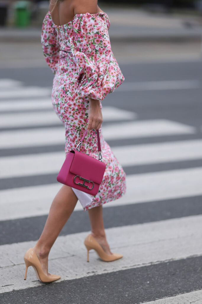 Жена облечена с рокля на розови цветя с буфан ръкави и розова чанта