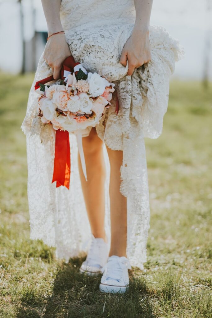 Жена облечена със сватбена рокля в бохо стил с букет в ръка, обута с ниски бели кецове
