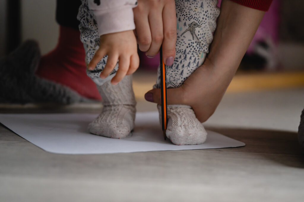 жена очертава на малко дете формата на стъпалата на хартиен лист